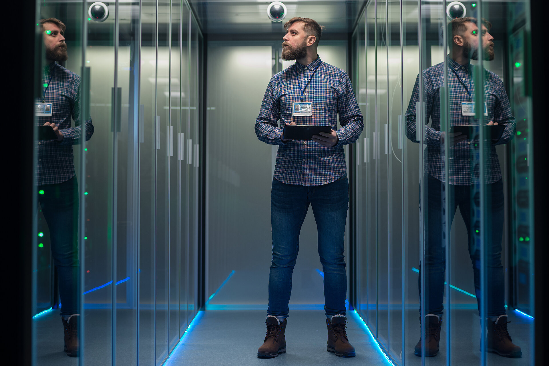 Mann steht in einem Rechenzentrum mit einem Tablet in der Hand, links und rechts Server