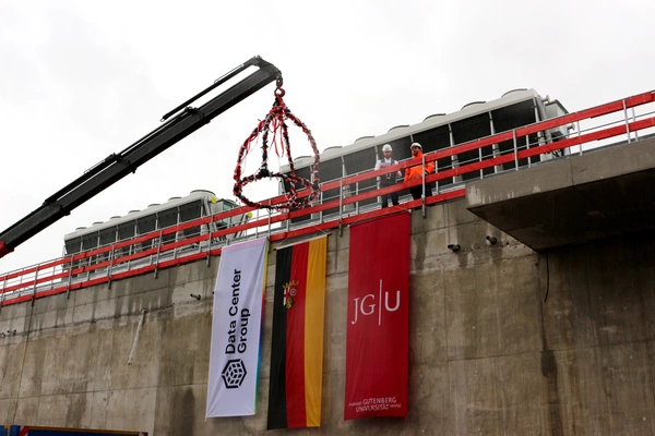 Dach des Rechenzentrums in Mainz mit Richtbaum, Fahnen der DCG, der JGU und Deutschland, sowie 2 Männer auf dem Dach, die etwas vorlesen