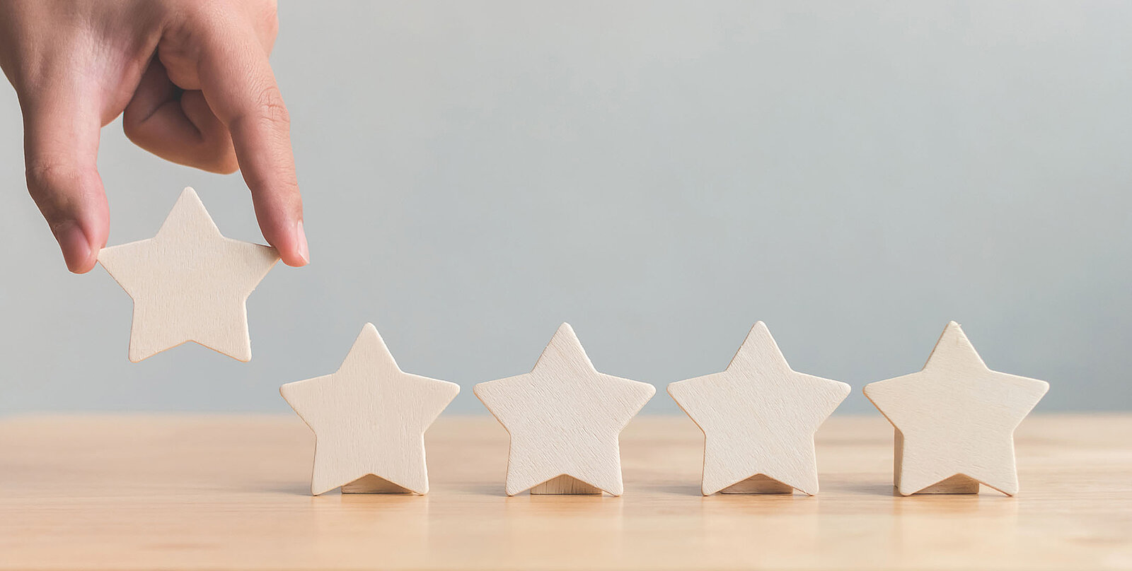 5 Sterne, wovon 4 auf einem Tisch stehen und der 5. Stern von einer Person auf den Tisch gelegt wird