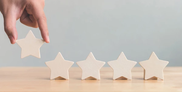 5 Sterne, wovon 4 auf einem Tisch stehen und der 5. Stern von einer Person auf den Tisch gelegt wird