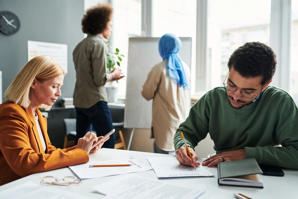 Four people are in an office, two are standing, two are sitting.