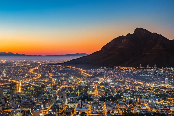 Blick auf eine Großstadt bei Abenddämmerung, dahinter ein Berg