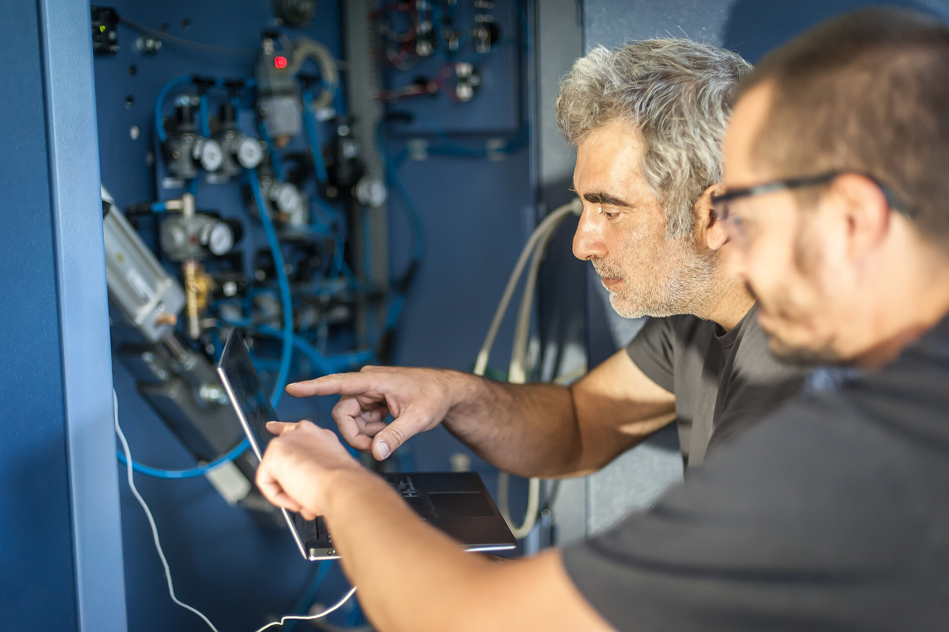 Zwei Techniker führen mit einem Laptop eine Systemprüfung an der elektrischen Anlage durch.
