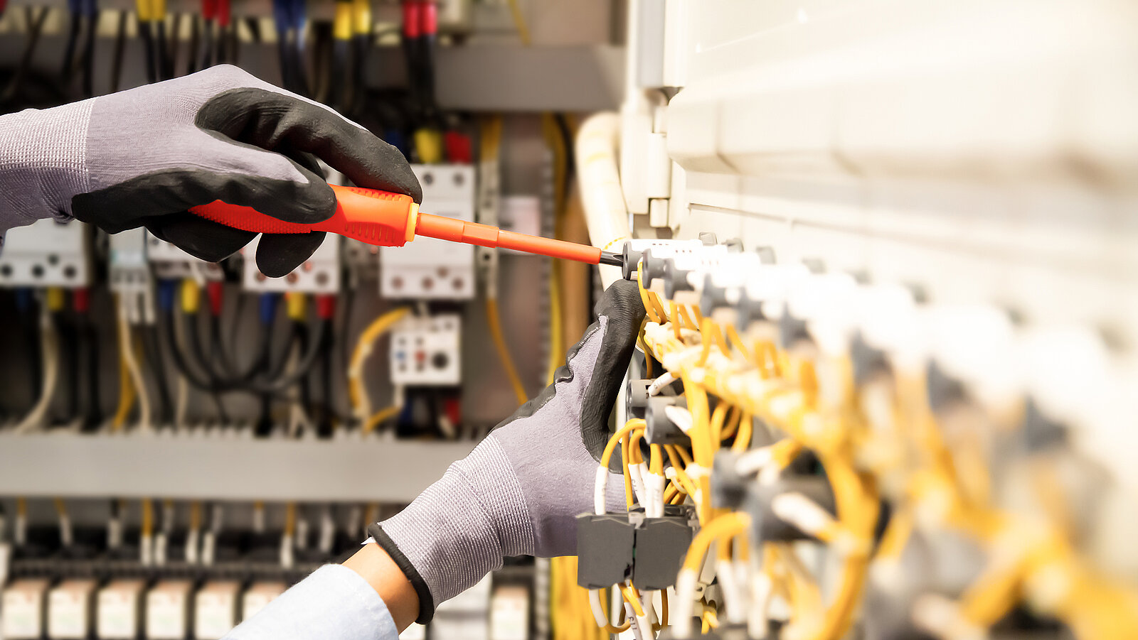 Eine Person mit Handschuhen tätigt mithilfe eines Schraubenziehers eine Elektroinstallation