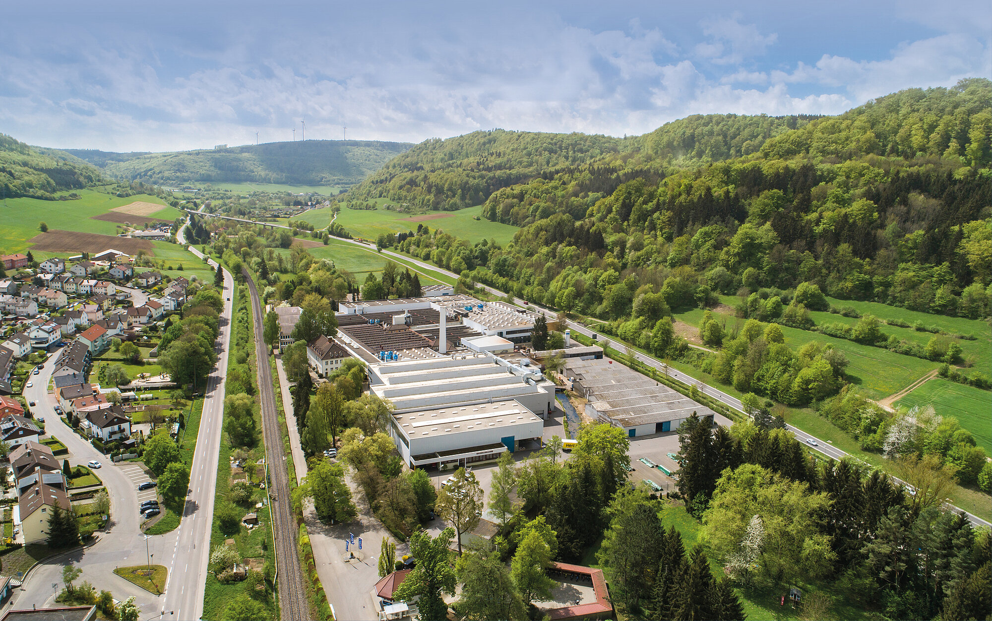 RUD Landschaft, in der Mitte Gebäude, links Häuser, rechts Wald und Grünfläche