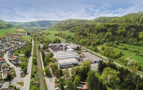 RUD Landschaft, in der Mitte Gebäude, links Häuser, rechts Wald und Grünfläche