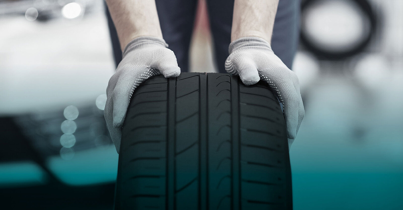 Ein Autoreifen, der von einer Person mit Handschuhen nach vorne gerollt wird