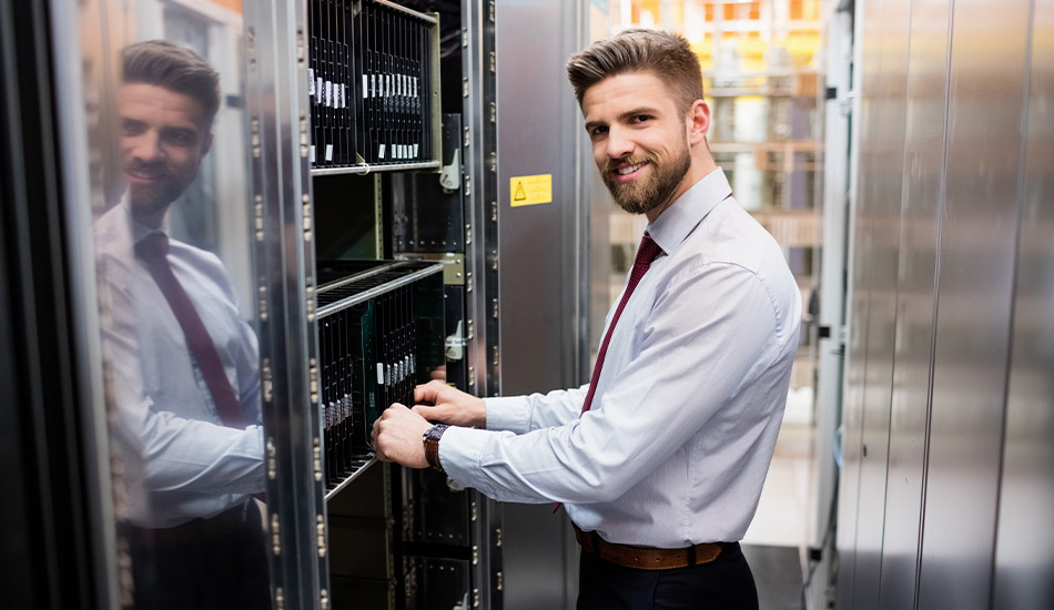 Lächelnder Mann vor Rechenzentrum hält ein Serverrack fest