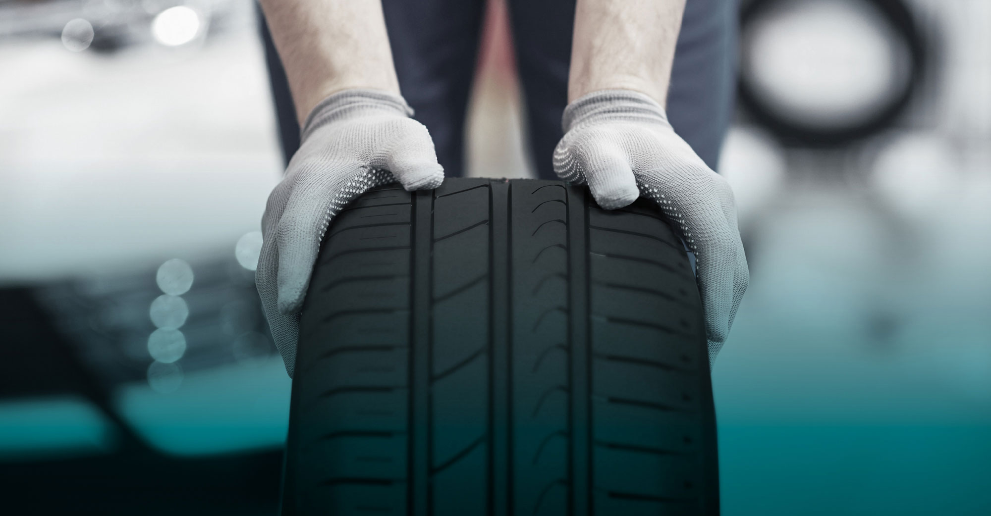 Ein Autoreifen, der von einer Person mit Handschuhen nach vorne gerollt wird
