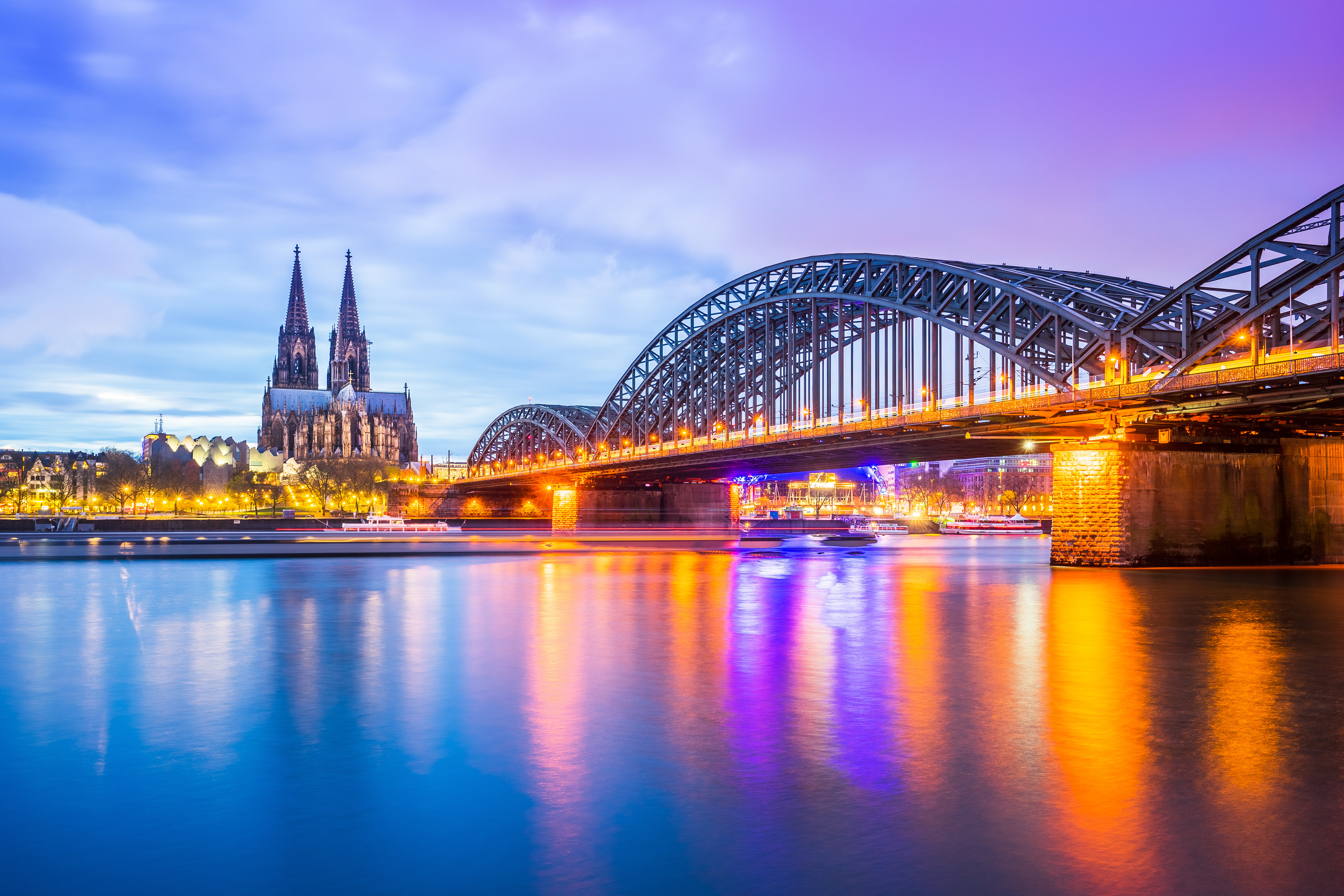 Skyline von Köln bei Dämmerung, mit dem Rhein und der Hohenzollernbrücke im Vordergrund und dem Kölner Dom im Hintergrund