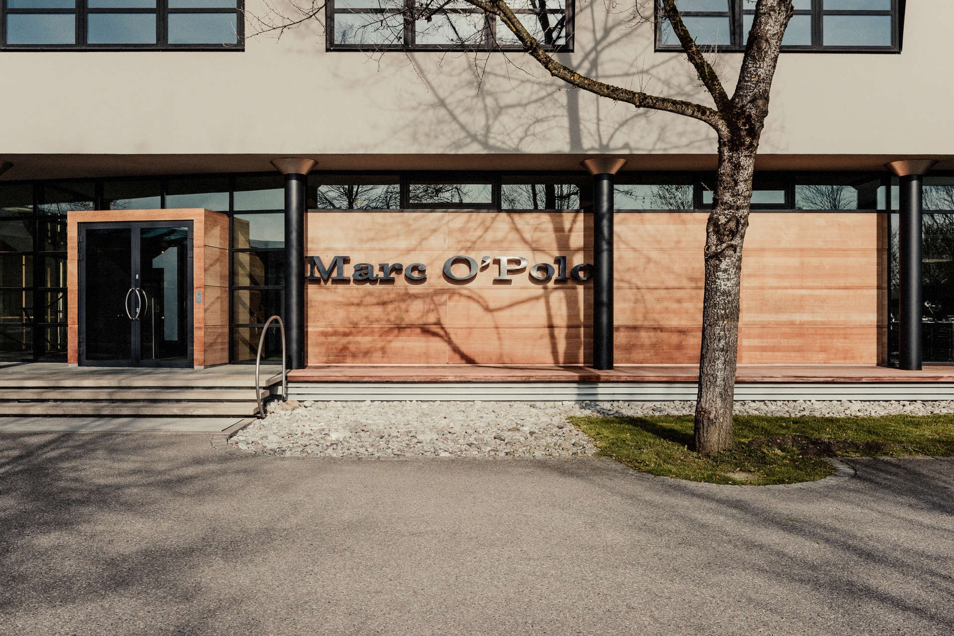 Building Marc O Polo with lettering in front, wooden facade, tree and street in front of it